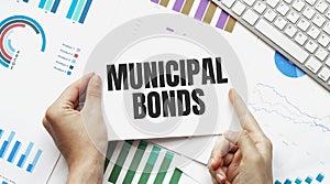 Businessman holding a card with text MUNICIPAL BONDS. Keyboard, diagram and white background