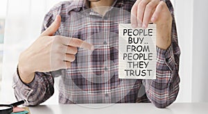businessman holding a card with text PEOPLE BUY FROM PEOPLE THEY TRUST, business concept image with soft focus