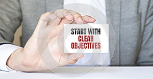 Businessman holding a card with text START WITH CLEAR OBJECTIVES