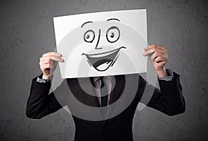 Businessman holding a cardboard with smiley face on it in front