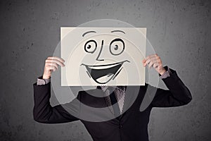 Businessman holding a cardboard with smiley face on it in front