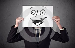 Businessman holding a cardboard with smiley face on it in front