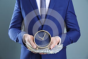 Businessman holding clock and money on color background. Time management