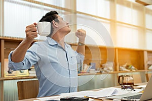 Businessman is holding coffee cup and stretching oneself while working at office