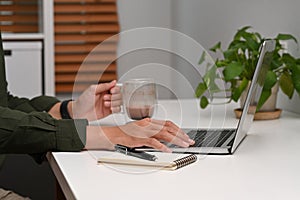 Businessman holding coffee cup and working with laptop computer at home office.