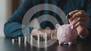 A businessman holding a coin in a piggy bank. Placing coins in a row from low to high is comparable to saving money to grow more.