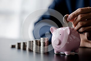 A businessman holding a coin in a piggy bank. Placing coins in a row from low to high is comparable to saving money to grow more.