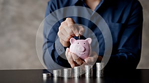 A businessman holding a coin in a piggy bank. Placing coins in a row from low to high is comparable to saving money to grow more.