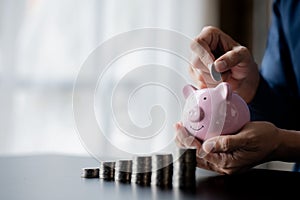 A businessman holding a coin in a piggy bank. Placing coins in a row from low to high is comparable to saving money to grow more.