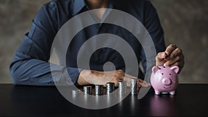 A businessman holding a coin in a piggy bank. Placing coins in a row from low to high is comparable to saving money to grow more.