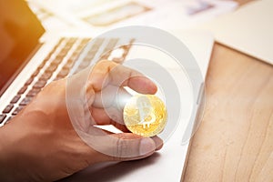 Businessman holding cryptocurrency golden bitcoin coin in hand with computer laptop at background. crypto currency,
