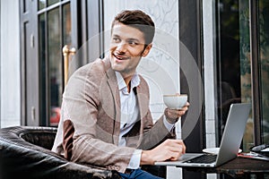 Businessman holding cup of coffee and working with laptop outdoors