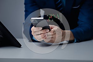 Businessman holding a device with a stock chart hologram, investing, using technology to invest in stocks. The concept of using