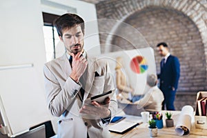 Businessman holding digital tablet with team discussing project in the background