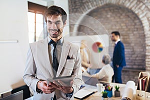 Businessman holding digital tablet with team discussing project in the background