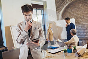 Businessman holding digital tablet with team discussing project in the background