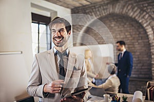 Businessman holding digital tablet with team discussing project in the background