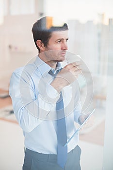 Businessman holding disposable cup and tablet looking out the window