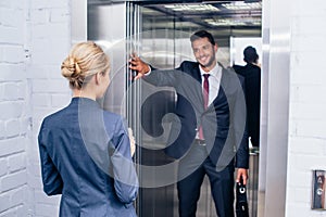 Businessman holding elevator door for woman