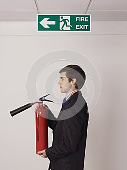 Businessman Holding Fire Extinguisher Under Exit Sign