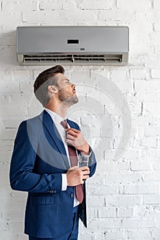 Businessman holding glass of water while standing under air conditioner