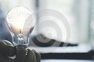 Businessman holding glowing lightbulb with brain and using computer laptop to input business strategy idea , creative thinking