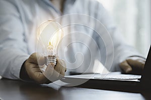 Businessman holding glowing lightbulb and using computer laptop to input business strategy idea , creative thinking ideas and