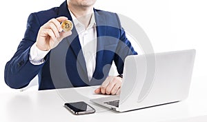 Businessman holding golden bitcoin while working with laptop and phone at table over white background