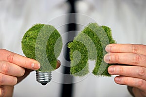 Businessman holding green eco light bulb with grass and miniature house.