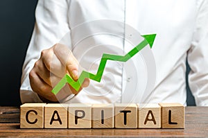 A businessman is holding a green up arrow above the word Capital. Increasing the attractiveness of the conditions for business
