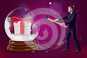 A businessman holding a hammer and crashing a big crystal ball with a gift box inside on a purple background with a few