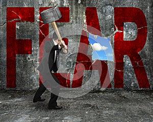 businessman holding hammer hitting red FEAR word on concrete wall