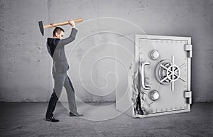 Businessman holding hammer over his head, and safe with its door broken