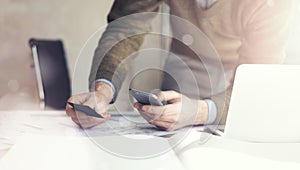 Businessman holding hand businesscard and making photo smartphone. Architectural project on the table. Horizontal mockup