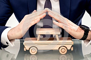 Businessman holding hands above the wooden auto. Professional car insurance solution for the best protection