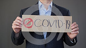 Businessman holding hands poster with sign covid-19 while world pandemic. Male hands showing nameplate with crossed