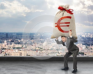 Businessman holding heavy moneybag with euro sign