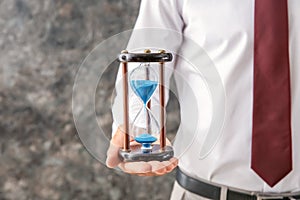 Businessman holding hourglass on grey background, closeup. Time management concept