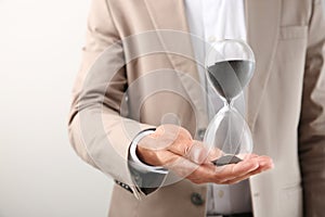 Businessman holding hourglass on light background, closeup. Time management concept