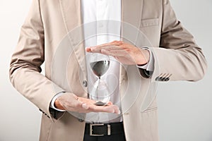 Businessman holding hourglass on light background. Time management concept