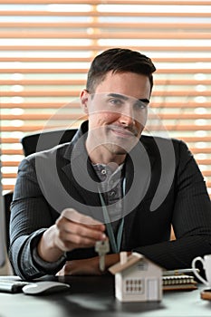 Businessman holding house keys and smiling to camera. Mortgage and real estate investment concept.