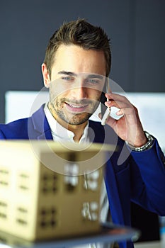 Businessman holding house miniature on hand standing in office.