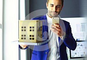 Businessman holding house miniature on hand standing in office.