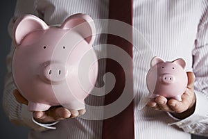 Businessman Holding Large And Small Piggy Bank