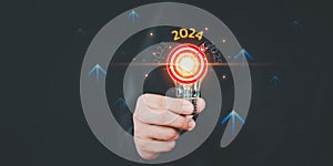 Businessman holding a light bulb with goal icon and the year 2024.