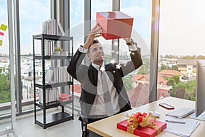 Businessman holding and looking red gift box with falling magic stars in office - Christmas and Happy ne