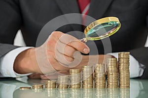 Businessman Holding Magnifier On Coin At Desk