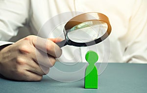 A businessman is holding a magnifying glass over a green man figure. Search for a talented employee. Identifying strengths in the