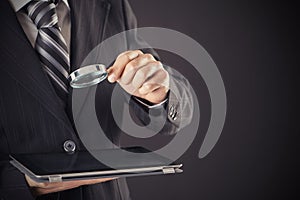 Businessman holding magnifying glass and tablet