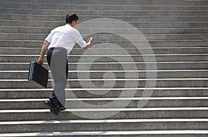 Businessman holding mobile and in hurry to run up on stairs